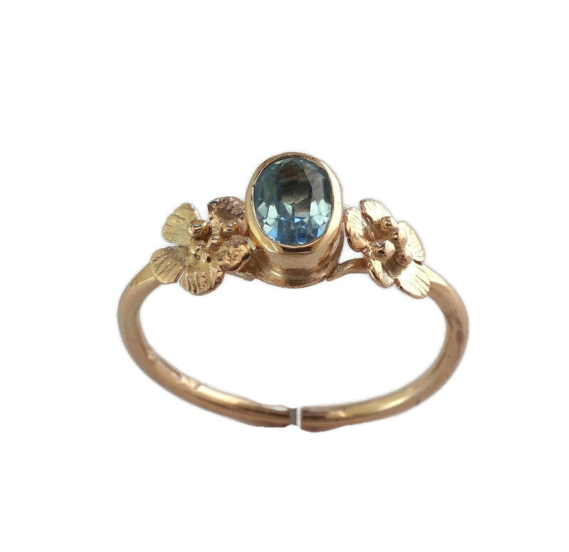 yellow gold ring with two flowers either side of the central oval blue topaz