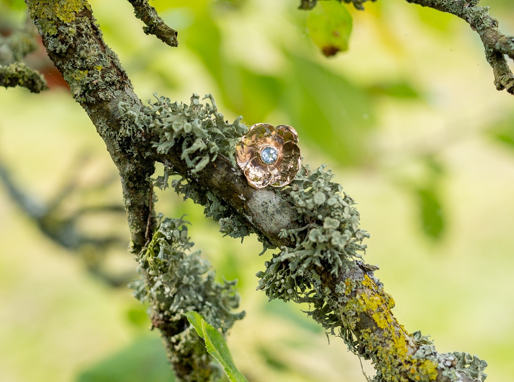 large yellow gold rose ring with blue gemstone center resting on mossy branch