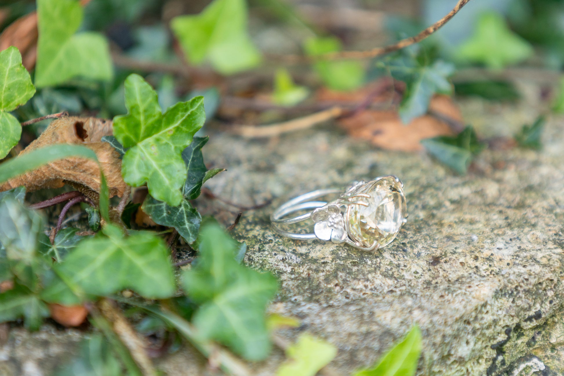 large yellow citrine stone floral cocktail ring, resting on granite block with ivy  