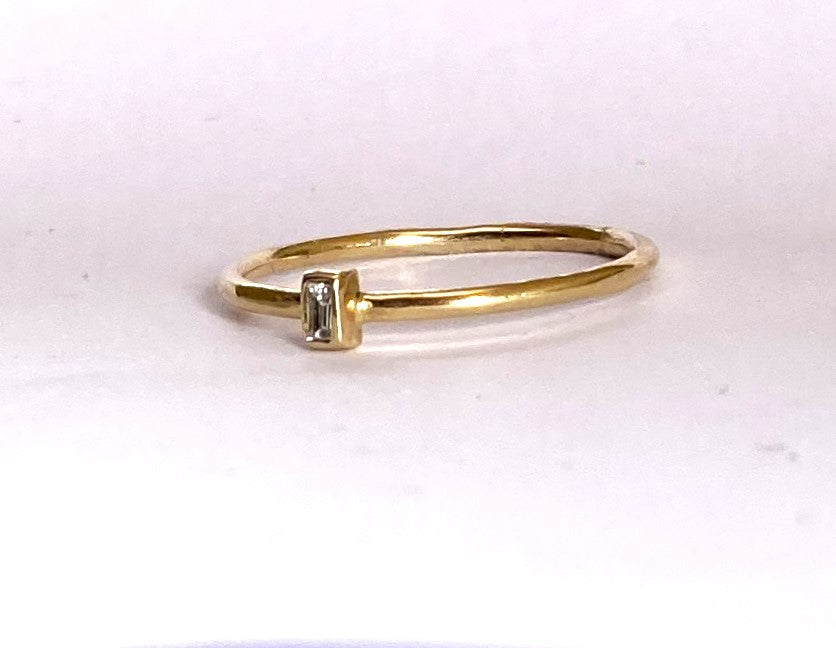 slim gold halo ring with small diamond baguette, on white background