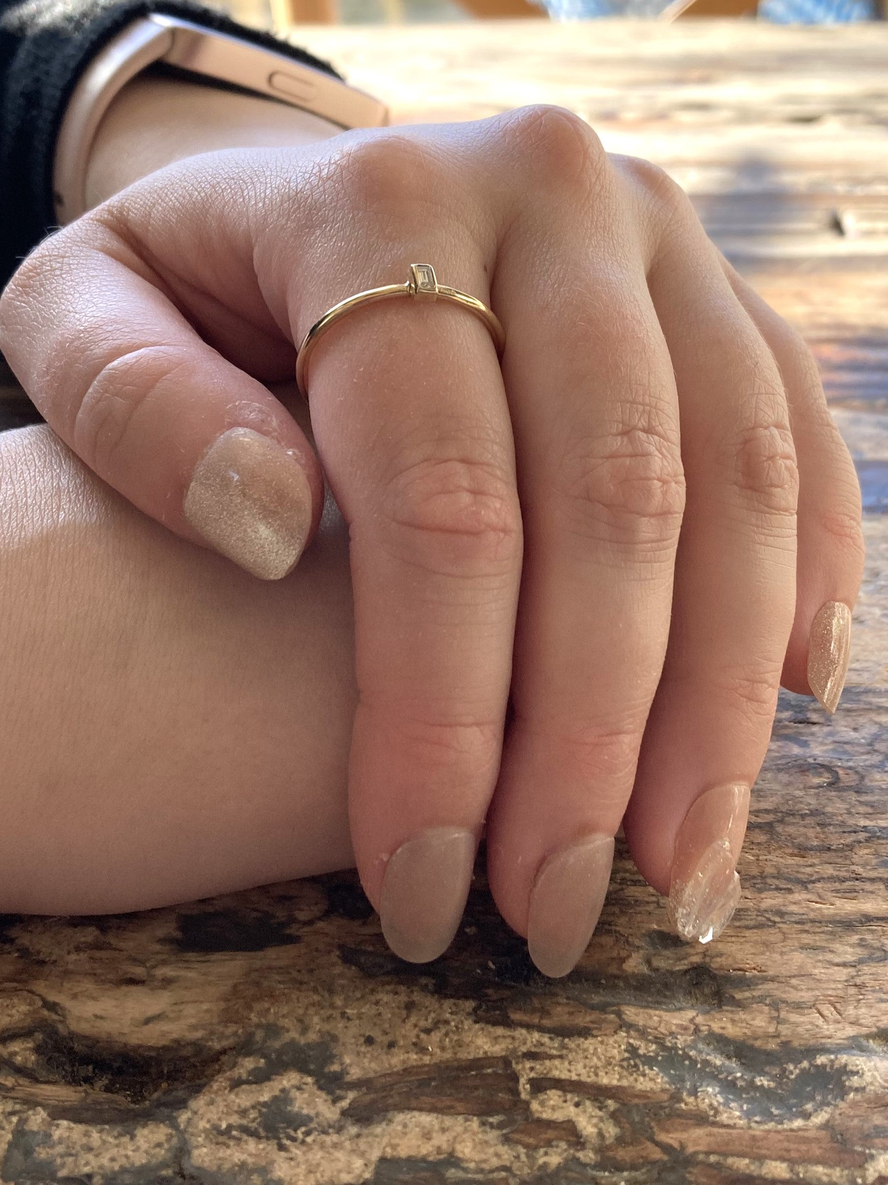 slim gold halo ring with oblong diamond, on ladies hand, on wood background