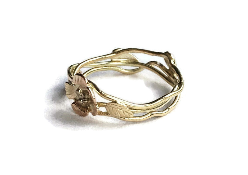 twisted gold wire ring with gold flower and engraved leaves on white background
