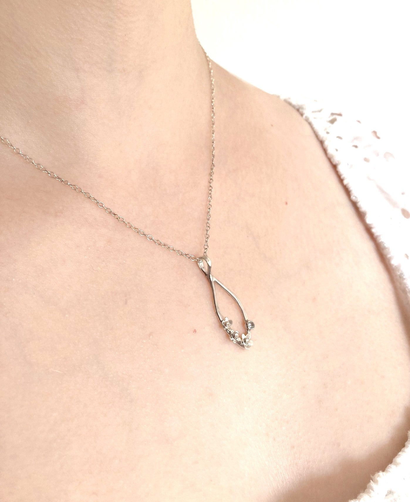 woman's neck wearing silver chain and simple floral drop pendant