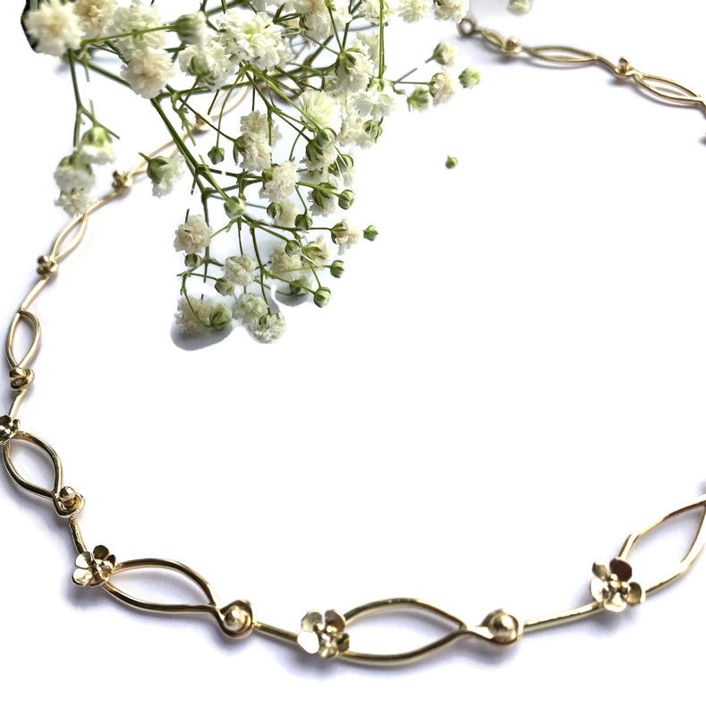 large link gold chain with little gold flowers, on white background with small bunch of white flowers