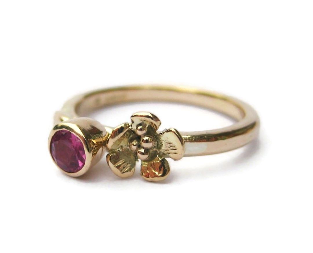 gold engagement ring with pink tourmaline gemstone and rose flower, on white background