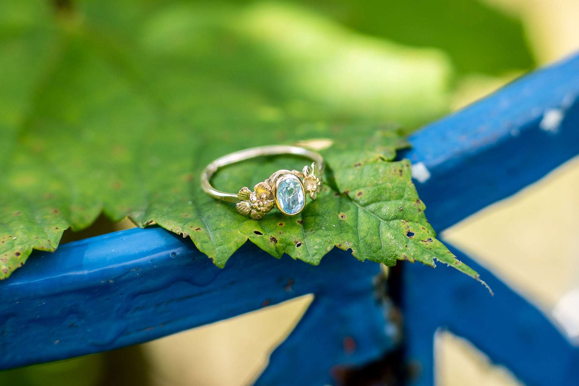 pale blue stone in gold ring resting on leaf with blue metal background