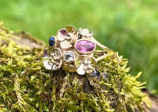 gold ring with tiny flowers and pink and blue gemstones resting on moss