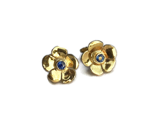hand cut yellow gold floral earrings set with central blue sapphire on white background