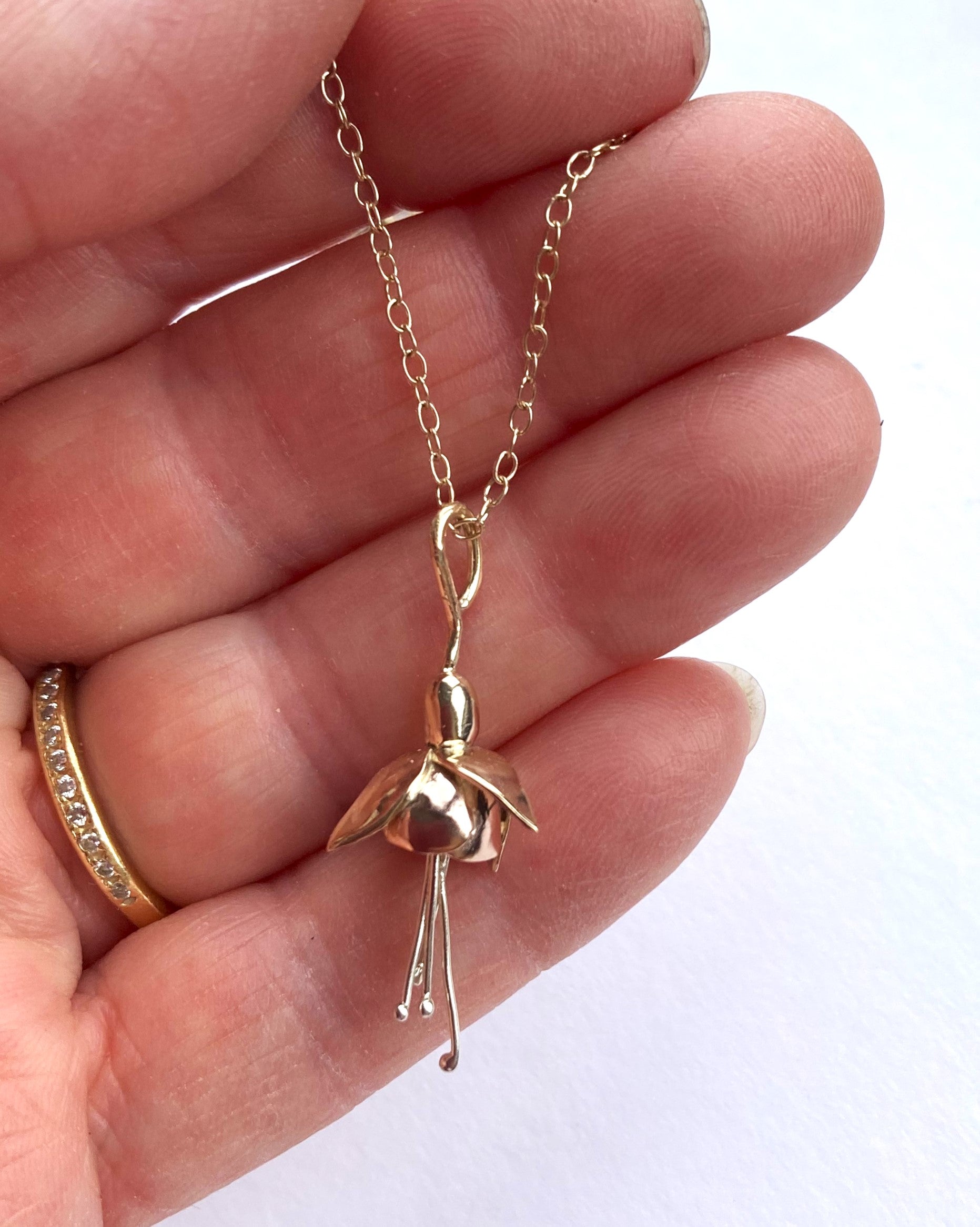 three colour gold fuchsia pendant resting on fingers