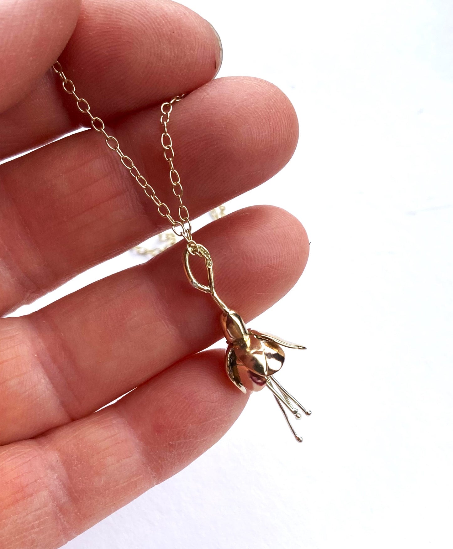 Small gold fuchsia pendant held on fingers