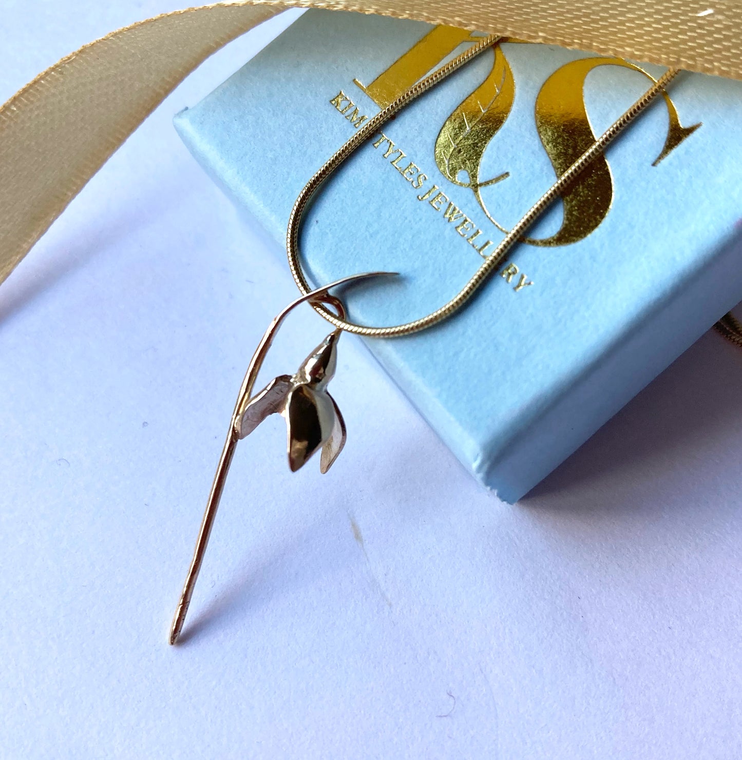 botanical gold snowdrop pendant on gold snake chain, resting on pale blue box with gold Kim Styles Jewellery logo, with gold ribbon