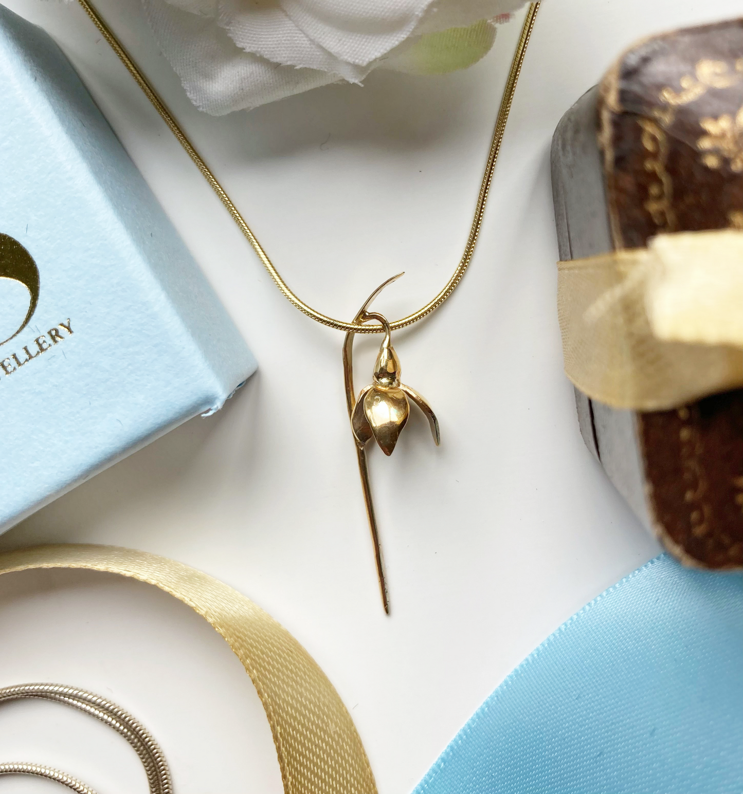 gold snowdrop pendant on gold snake chain, with blue and gold ribbon, pale blue box and vintage brown ring box