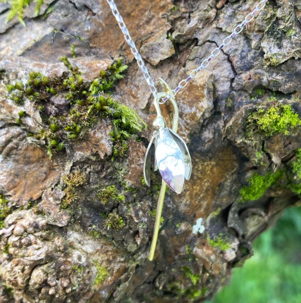 white gold snowdrop pendant and chain hanging on tree bark with moss