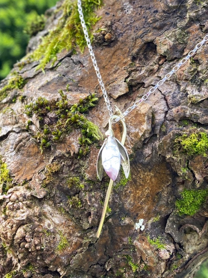 handmade snowdrop Galanthus pendant in green and white gold, on rough tree bark