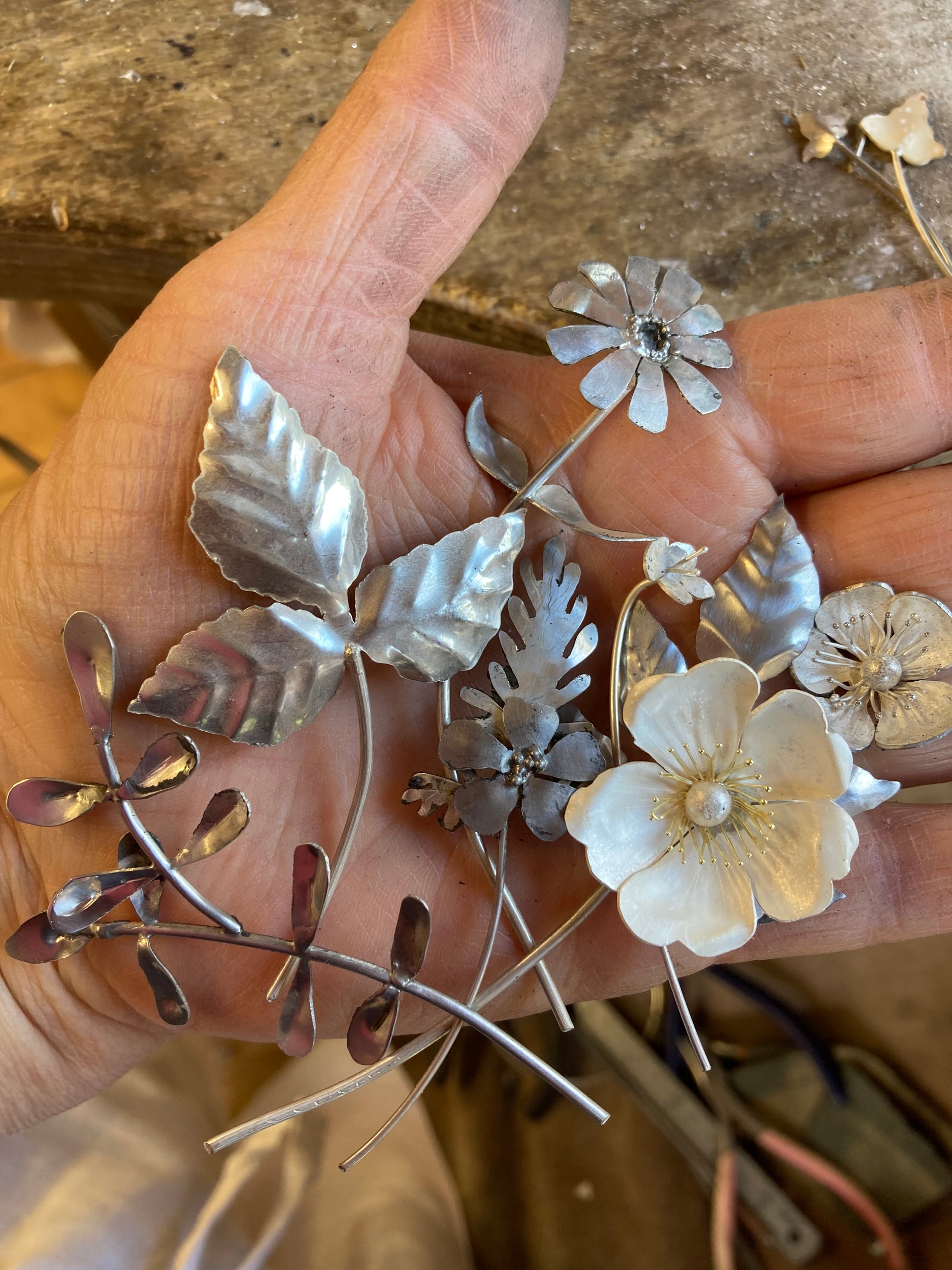 hand holding collection of hand forged sterling silver flowers and leaves