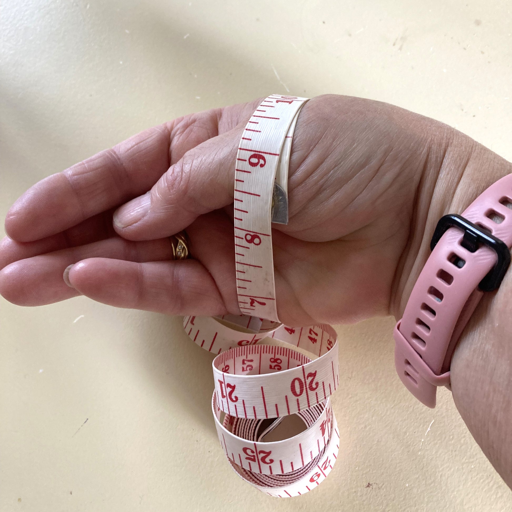 Hand with a measuring tape wrapped around it on a light background