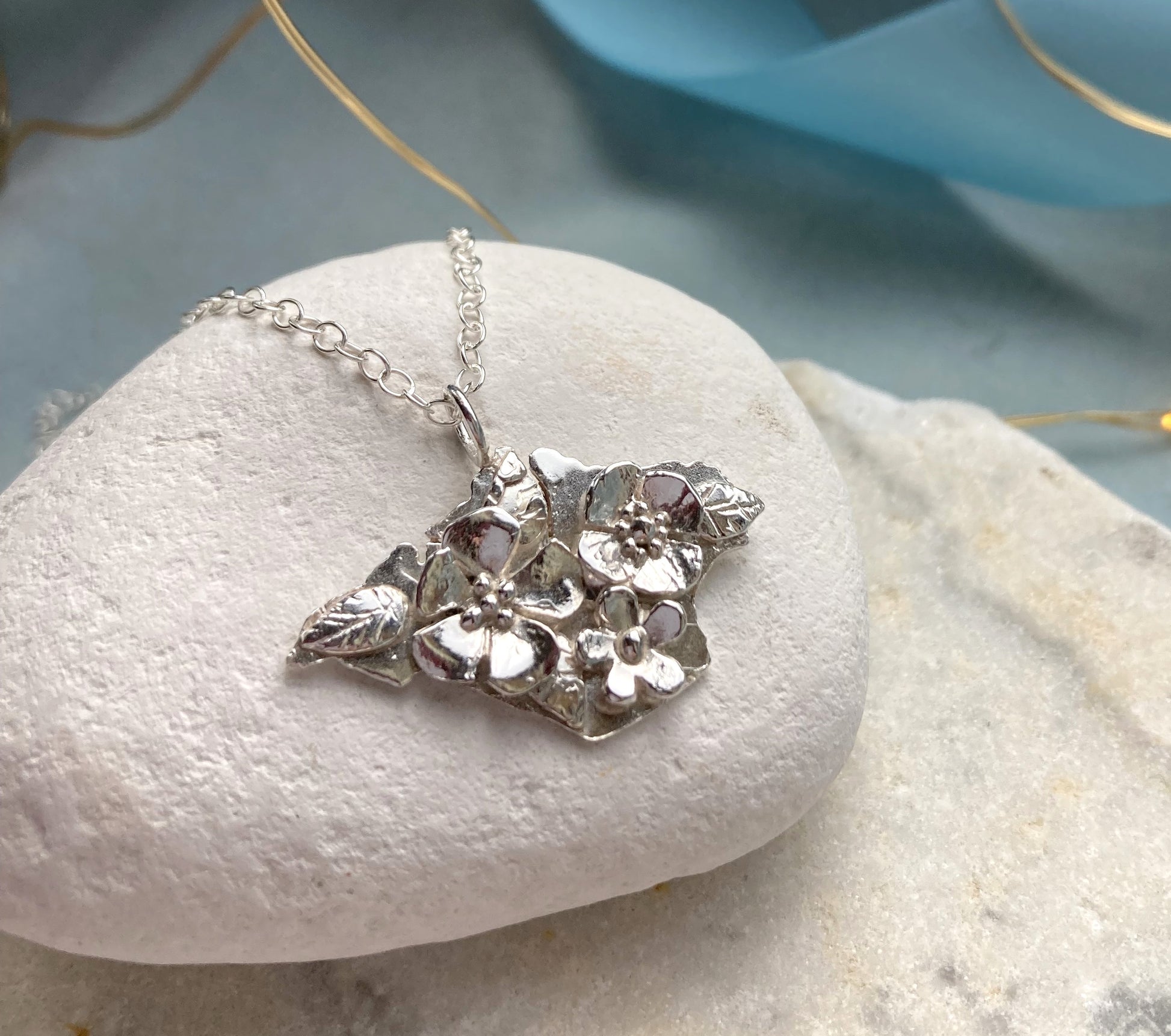 silver Isle of White shape pendant with flowers on surface, on white pebble
