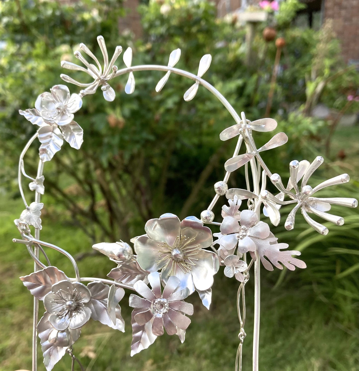 collection of wildflowers in shape of a wreath handmade in sterling silver with a green nature background