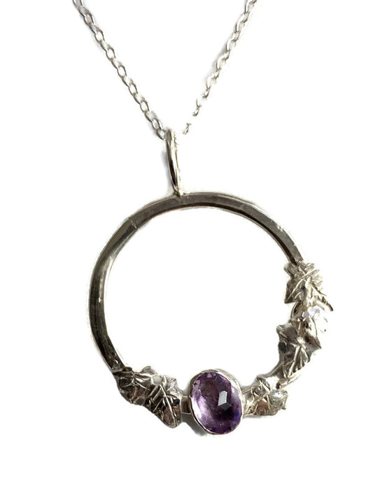 A silver necklace featuring a textured Ivy leaves open circular pendant with a faceted purple amethyst gemstone, shown against a plain white background.