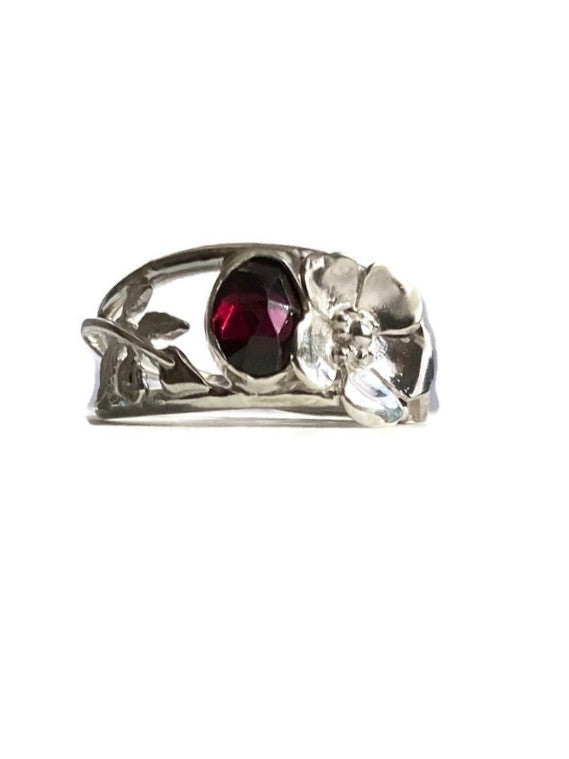 Floral asymmetrical cocktail ring with leaves and rose, set with oval red garnet gemstone, on plain white background