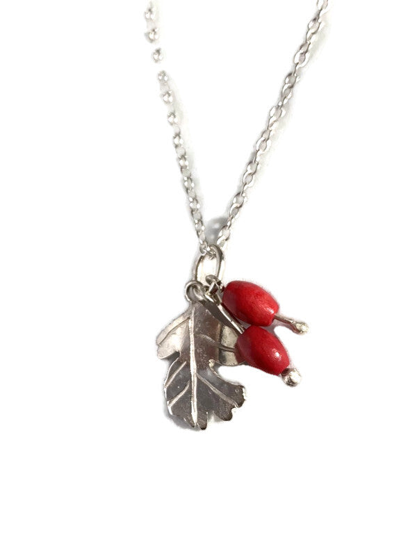 A silver chain necklace featuring a Hawthorne leaf with two hanging glossy red berries, on a plain white background.