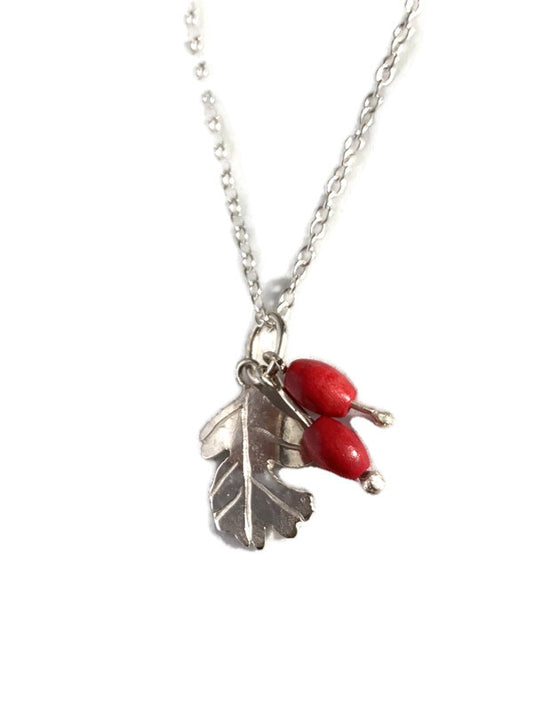 A silver chain necklace featuring a Hawthorne leaf with two hanging glossy red berries, on a plain white background.