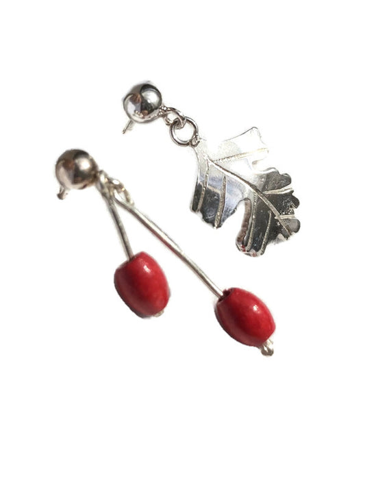 A pair of silver drop earrings featuring a leaf-shaped charm and red bead drops, shown against a plain white background.