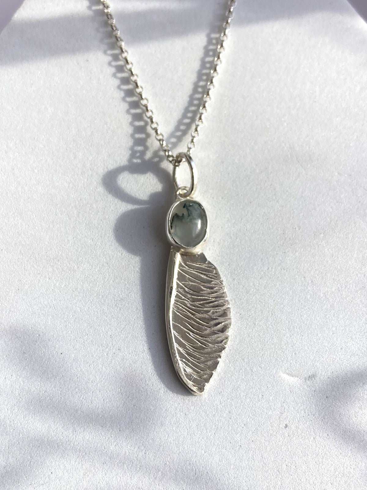 handmade textured silver sycamore seed pendant by Kim Styles Jewellery set with oval moss agate on grey background
