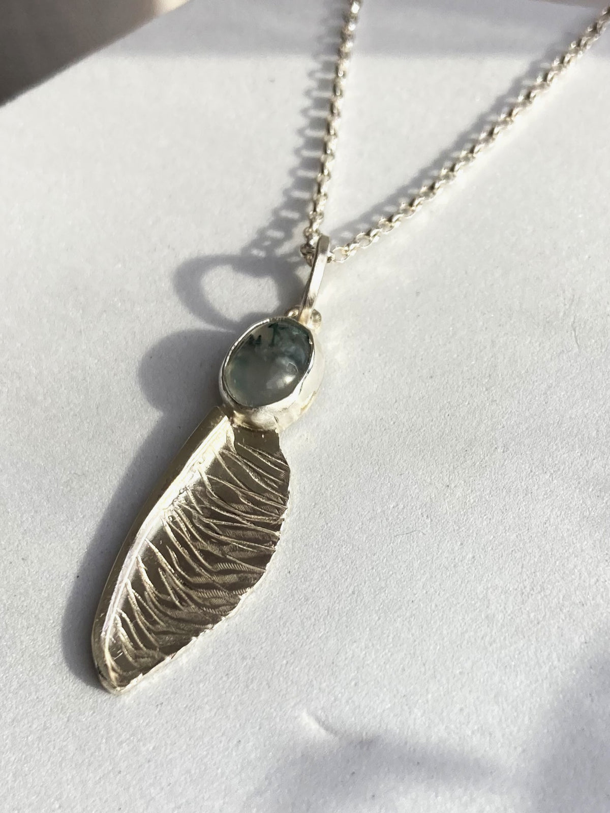 handmade textured  silver sycamore seed pendant by Kim Styles Jewellery set with oval green moss agate on white background