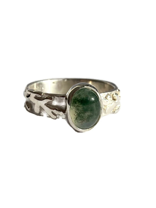 A sterling silver ring featuring an oval, polished green agate stone with natural marbling, set against a plain white background.