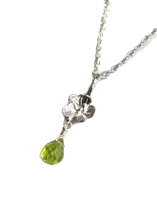 A silver floral pendant necklace featuring a small silver flower and a dangling faceted green peridot gemstone, shown on a plain white background.