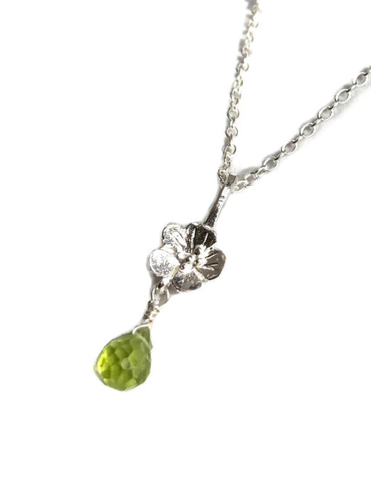 A silver floral pendant necklace featuring a small silver flower and a dangling faceted green peridot gemstone, shown on a plain white background.