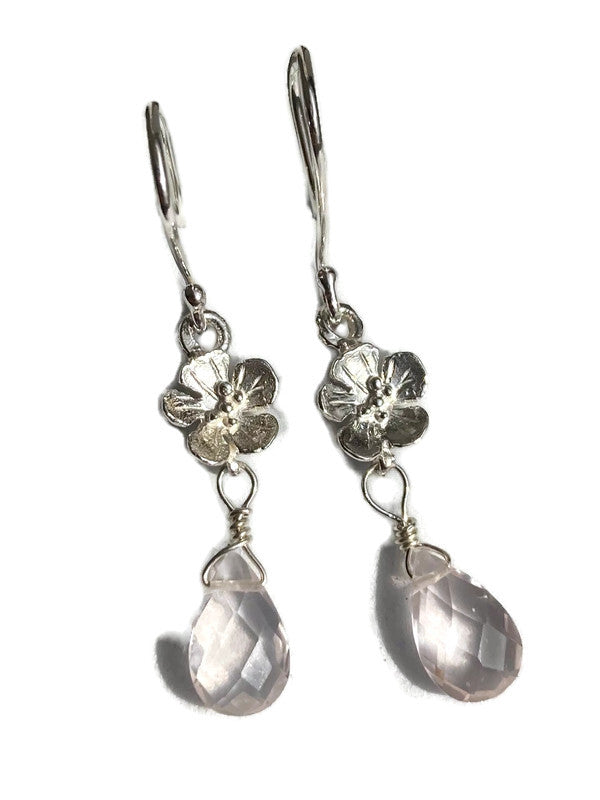 A pair of silver hook earrings featuring textured flower charms and faceted light pink teardrop gemstones, shown against a plain white background