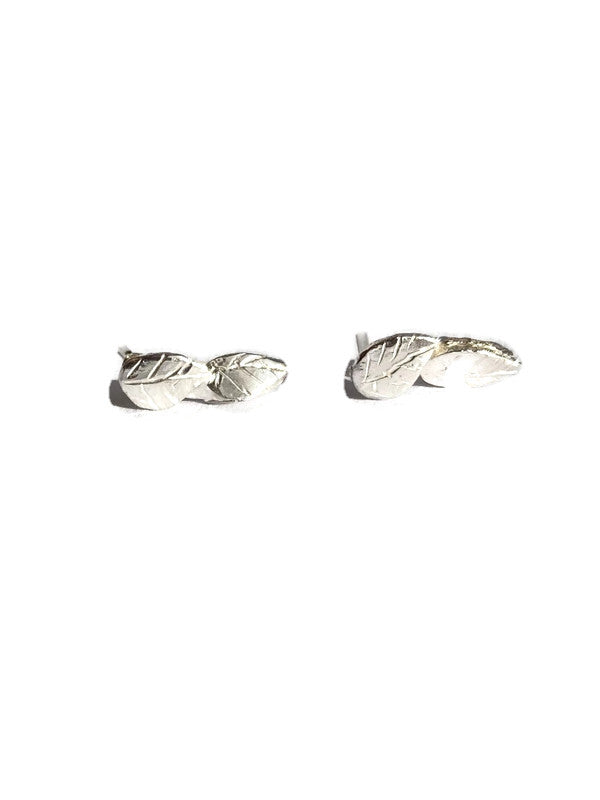 A pair of silver leaf stud earrings lying flat on a white background