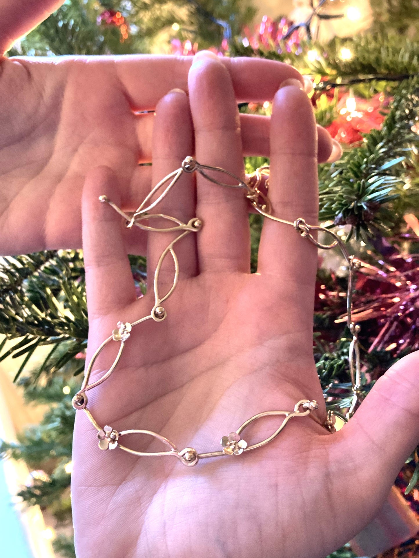 hands holding chunky hand made gold chain necklace with daisy details