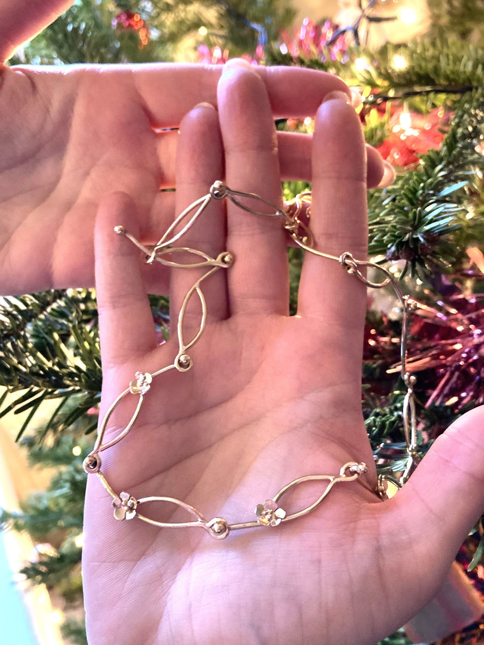 hands holding chunky hand made gold chain necklace with daisy details
