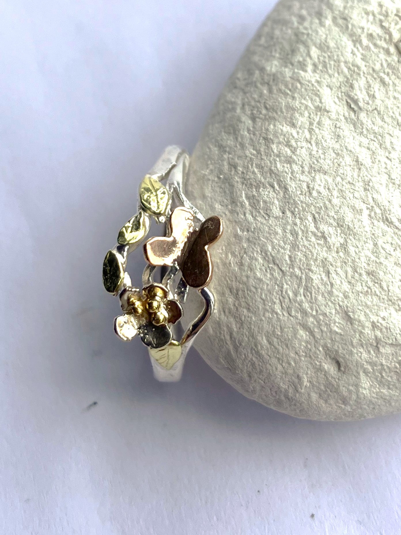 Silver ring with gold floral design and rose gold butterfly, by Kim Styles,  on a white stone background