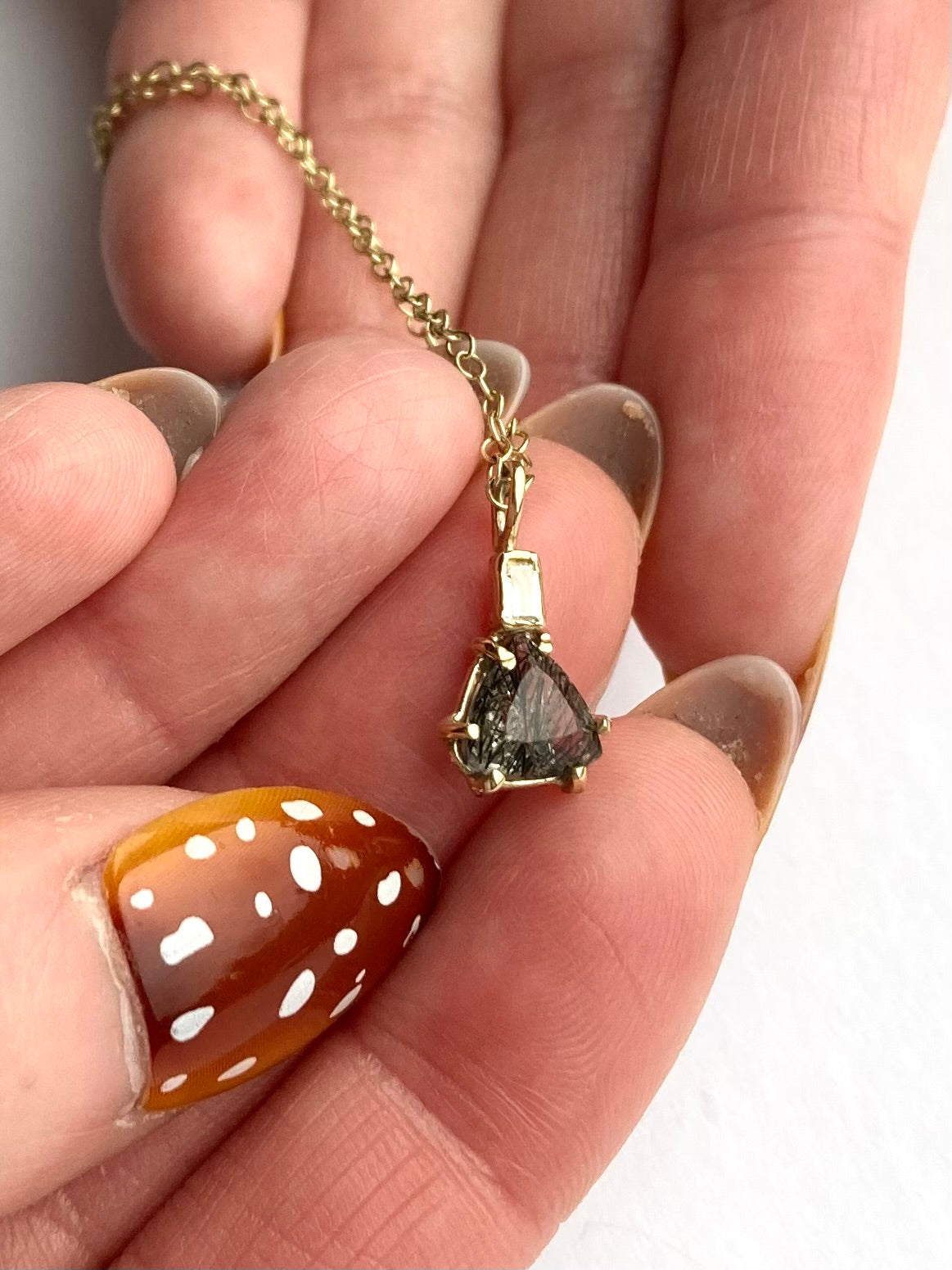 grey rutilated quartz trillion pendant with baguette diamond by Kim Styles Jewellery, held on fingers