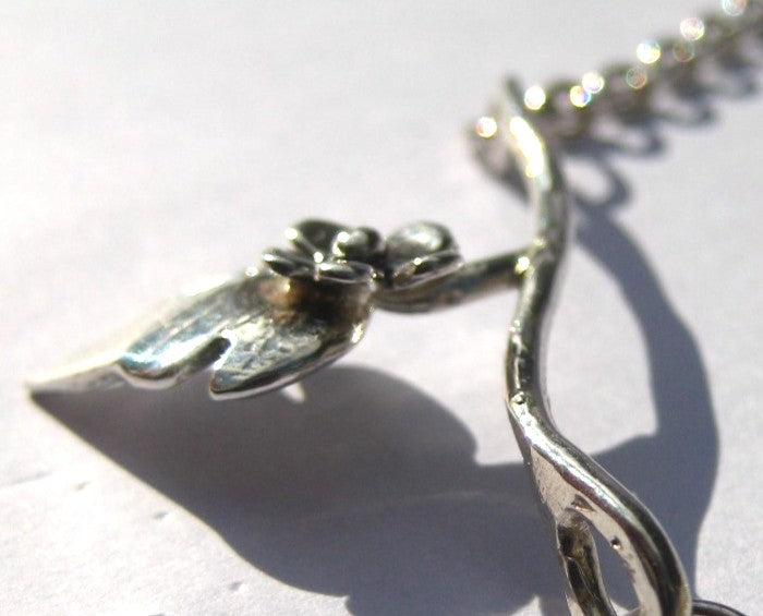 close up of silver flower and leaf necklace on white bakground