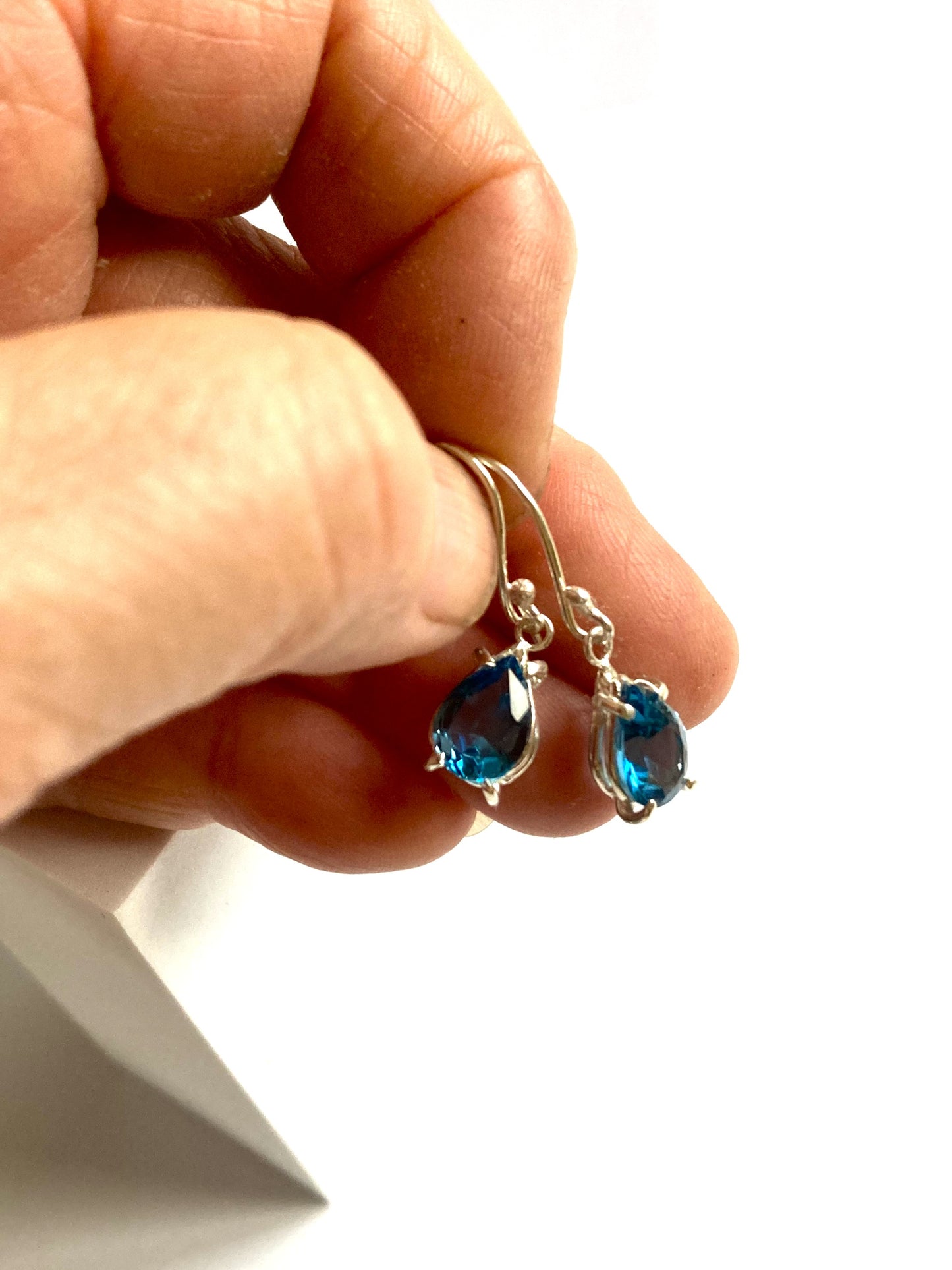 Hand holding a pair of silver earrings with blue London blue topaz against a white background