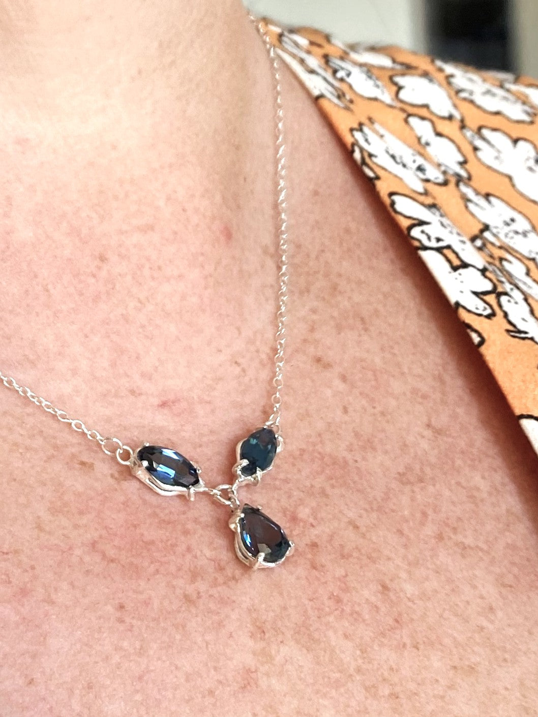 London blue topaz trio necklace on a person's neck, with a patterned fabric background