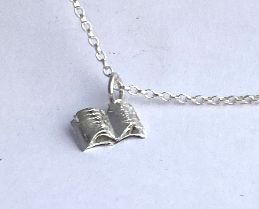 Tiny silver book pendant on grey background