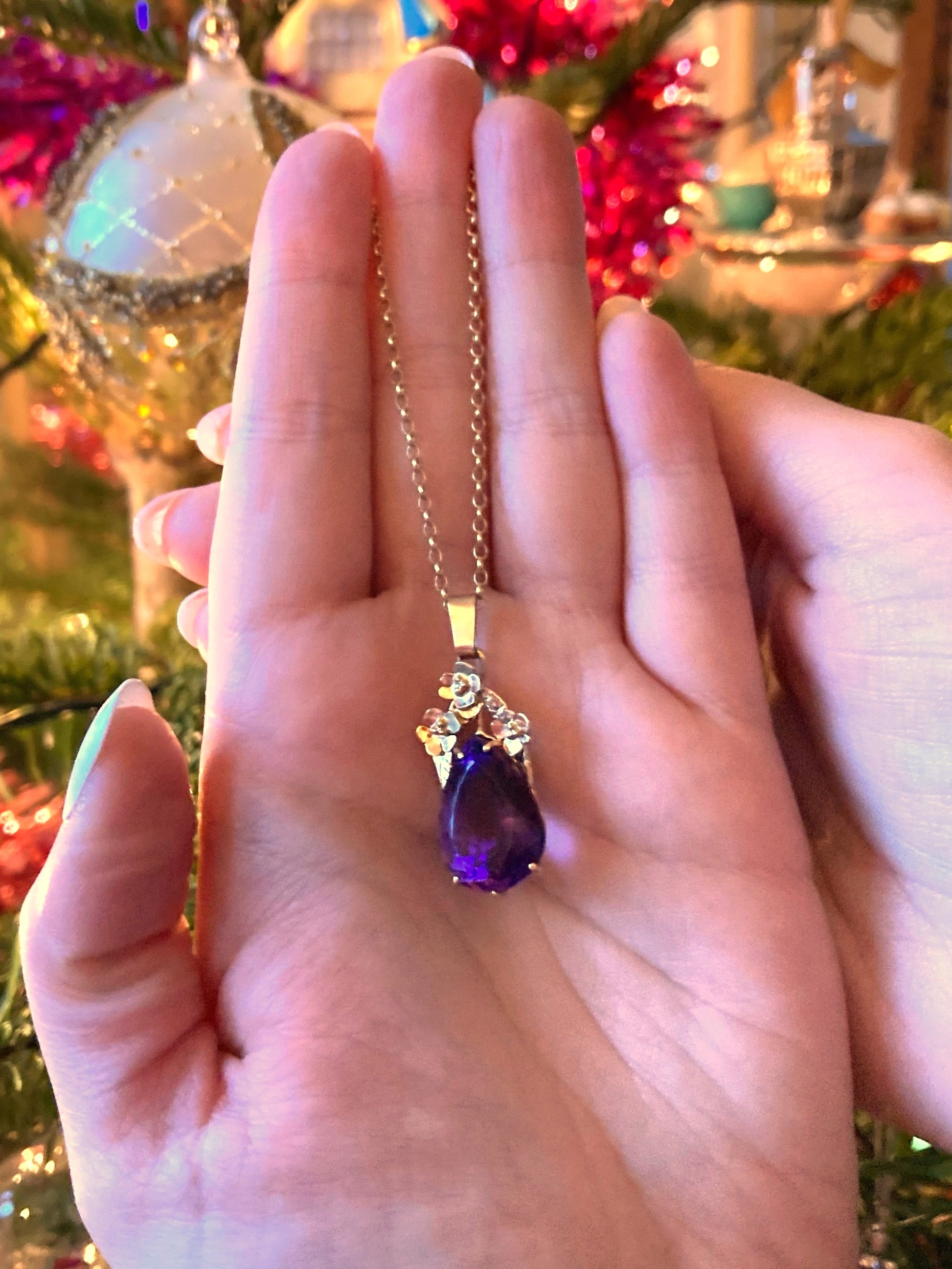 large pear shape amethyst gemstone set in gold, floral pendant and chain, on ladies hand