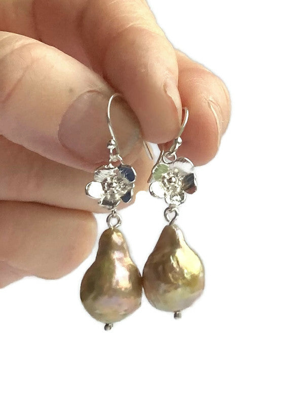 golden pear shape baroque pearl floral drop earrings held in fingers