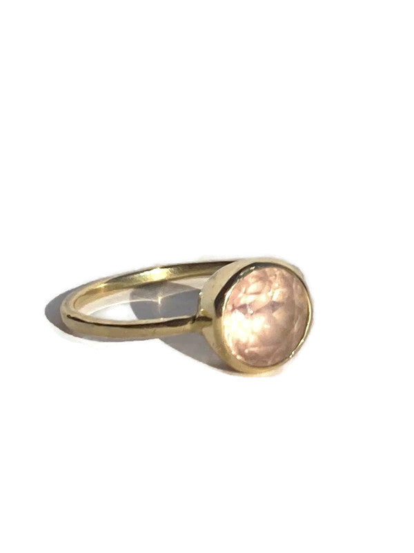 Gold ring with a pale pink round, textured stone on a white background