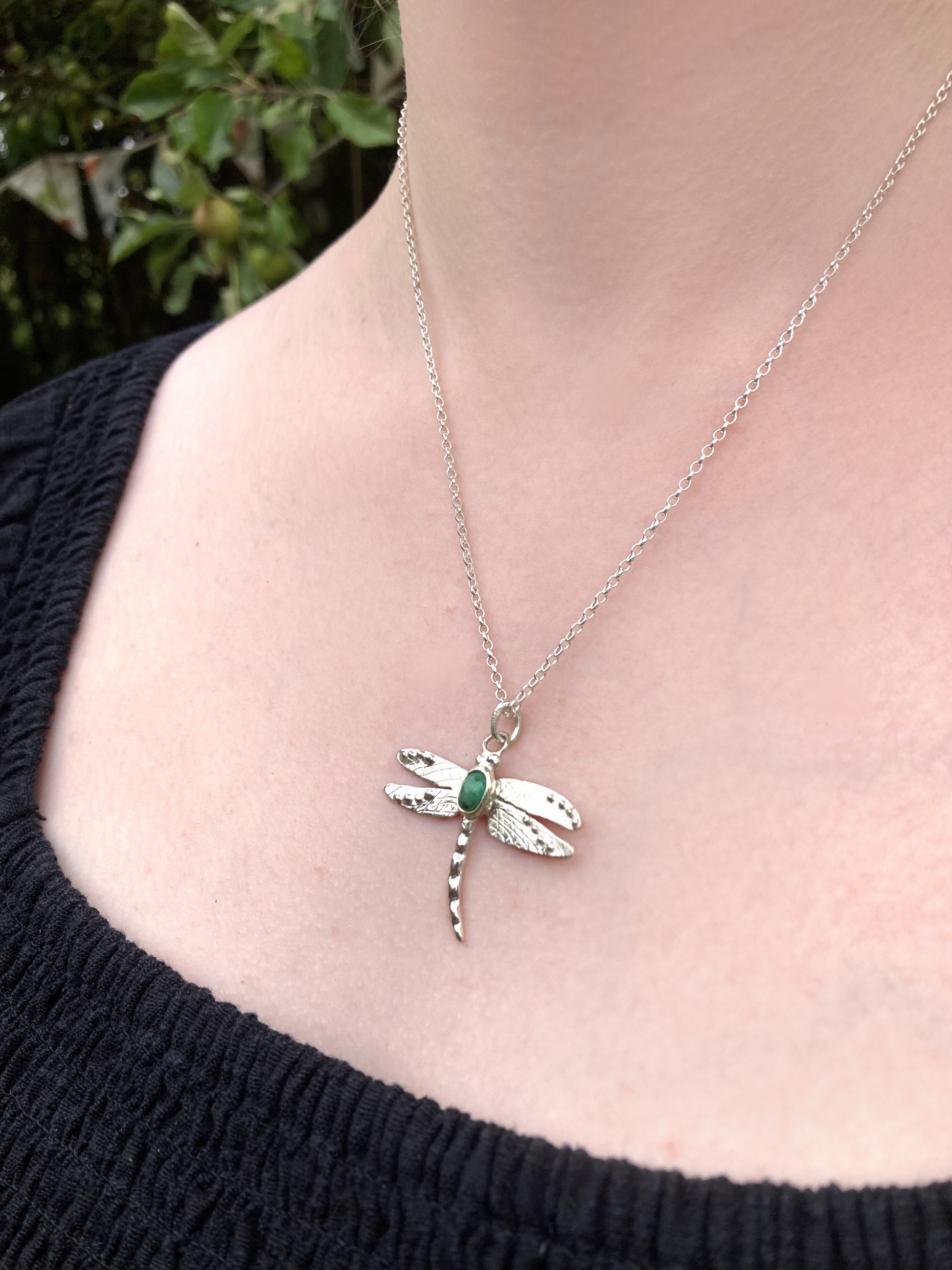 Emerald Dragonfly pendant necklace on a person with a blurred green background