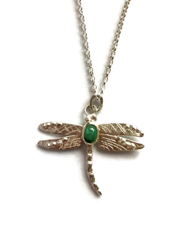 Dragonfly-shaped pendant with green cabochon emerald gemstone on a chain against a white background