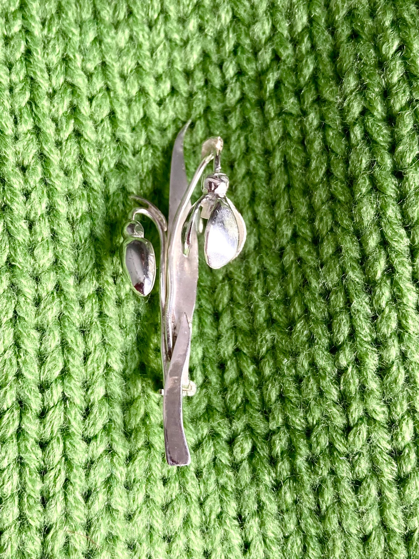Silver snowdrop flower brooch on a green knitted fabric background