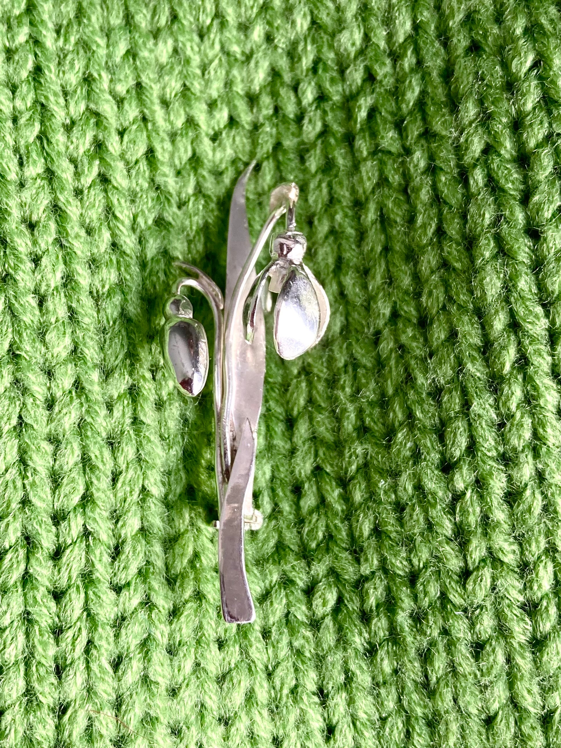 Silver snowdrop flower brooch on a green knitted fabric background