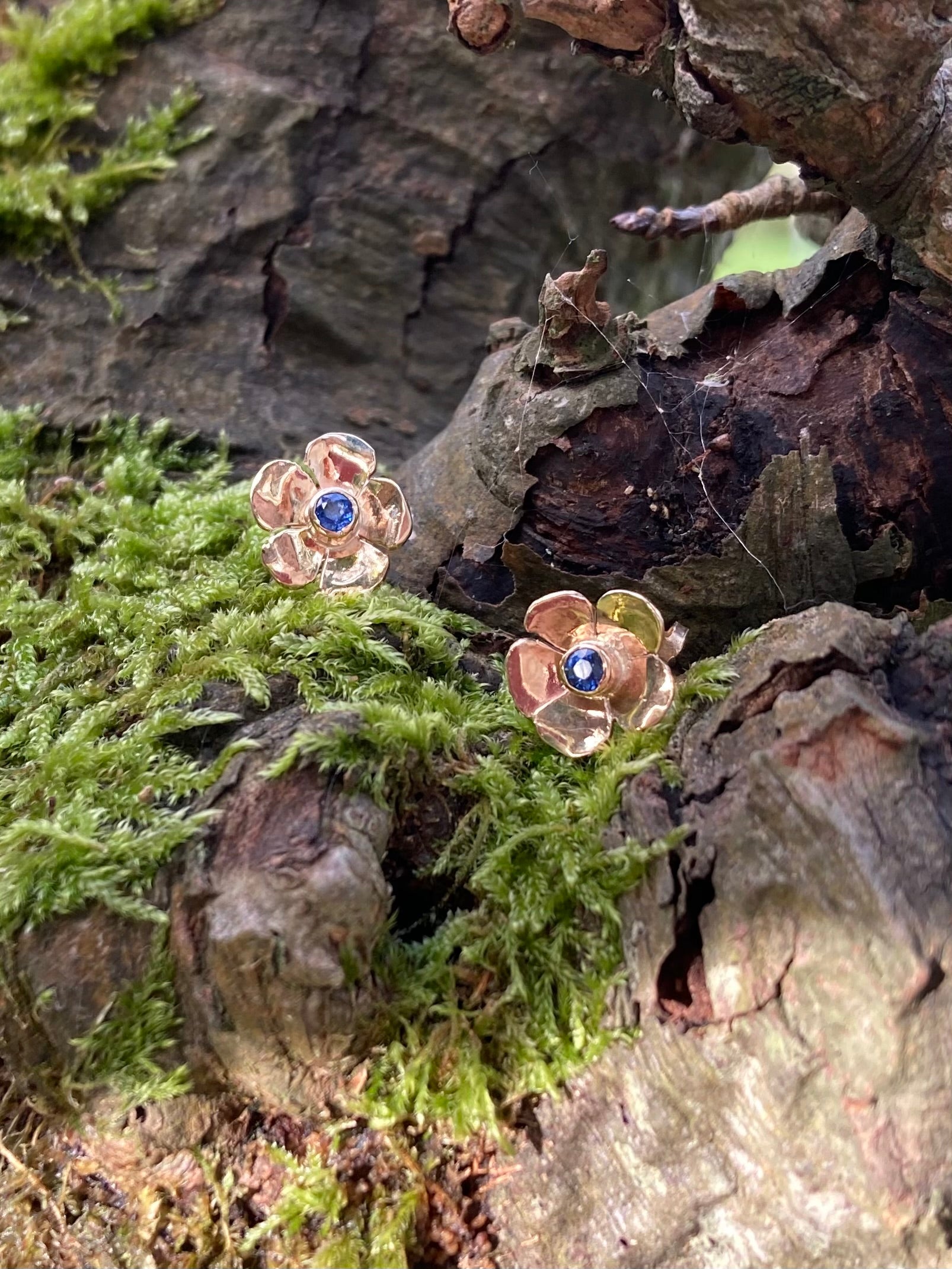 gold flower stud earrings set with bright blue sapphires on mossy tree